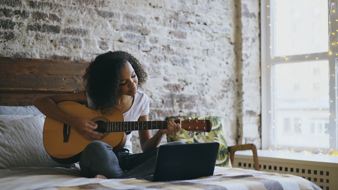Person learning to play acoustic guitar at home with chord chart visible