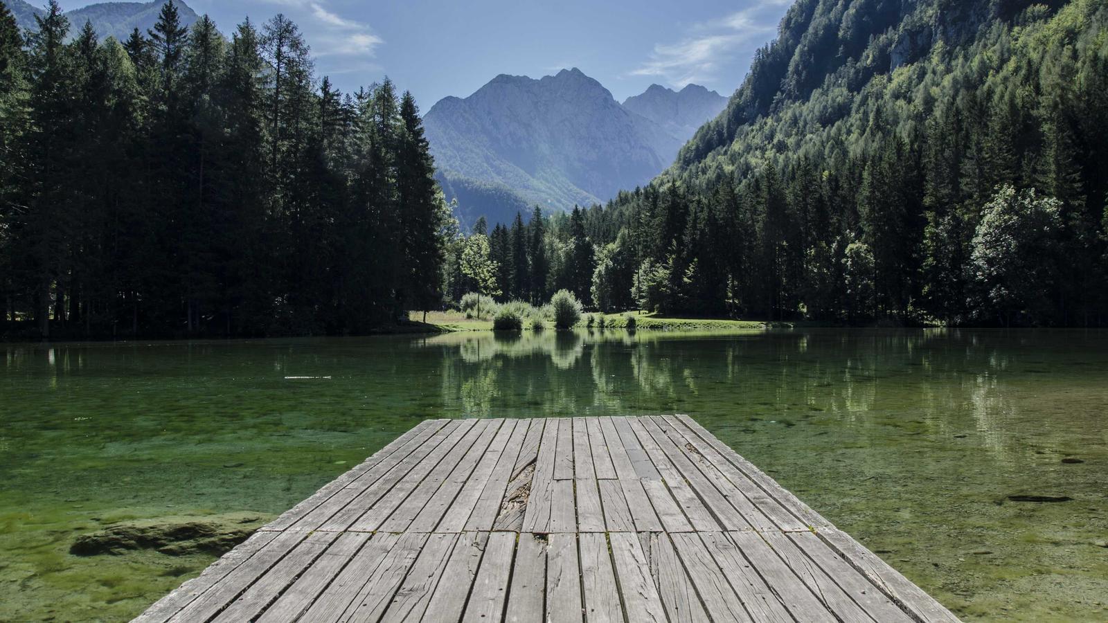 A contemporary opera production stage design with abstract geometric set pieces, minimal lighting and a single performer in dark contemporary costume standing at center stage with the orchestra pit visible.