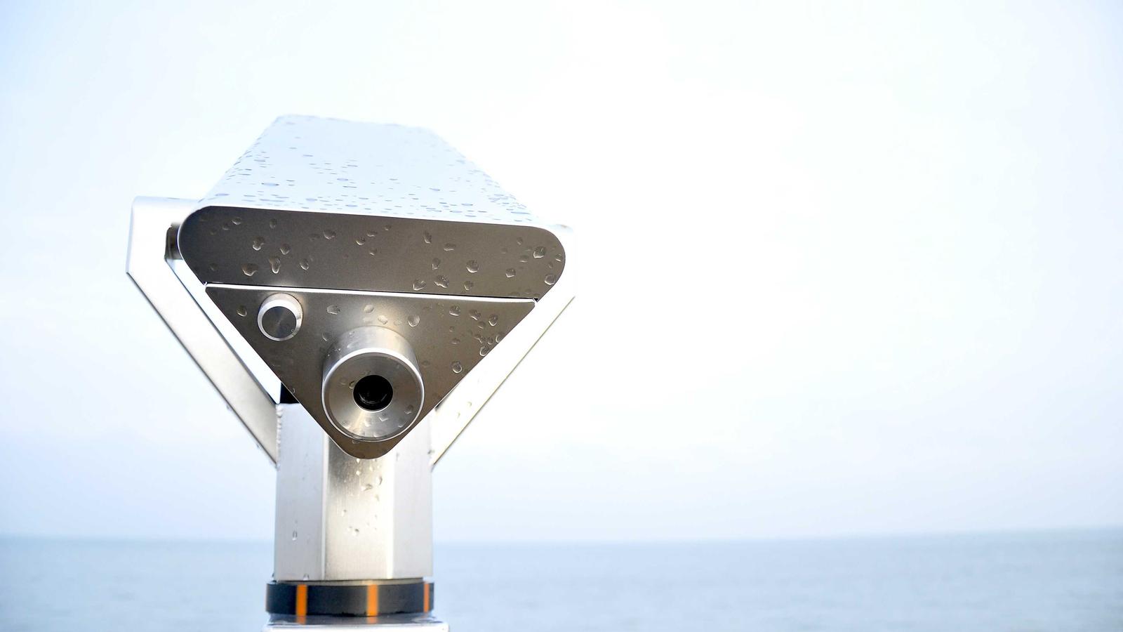 A musician's hands working at a modular synthesizer adjusting knobs with several brightly coloured patch cables visible in the foreground, in soft studio lighting with a small mixer beside the modular case.