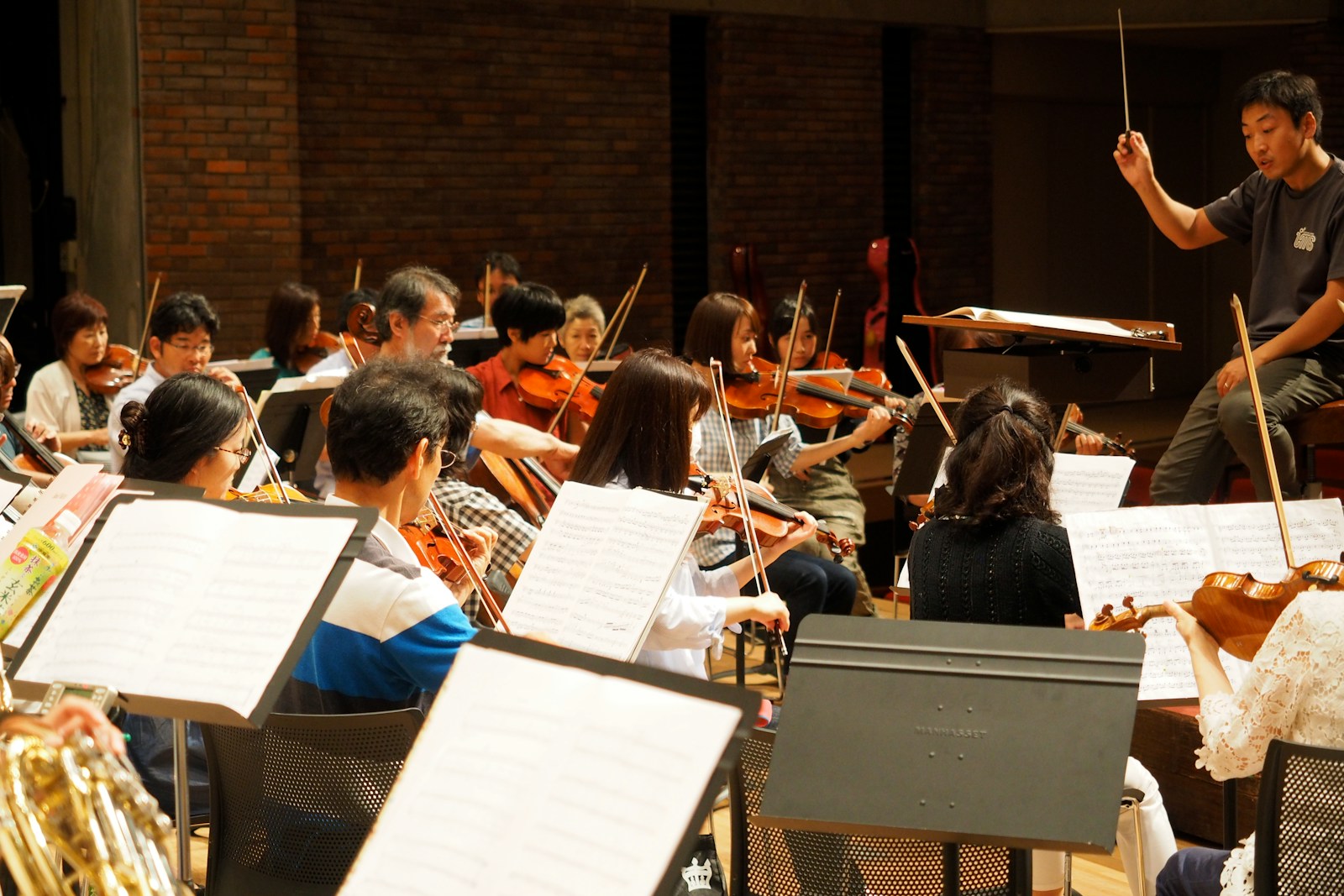 A chamber ensemble performing on a concert hall stage under warm lighting, audience visible in the foreground