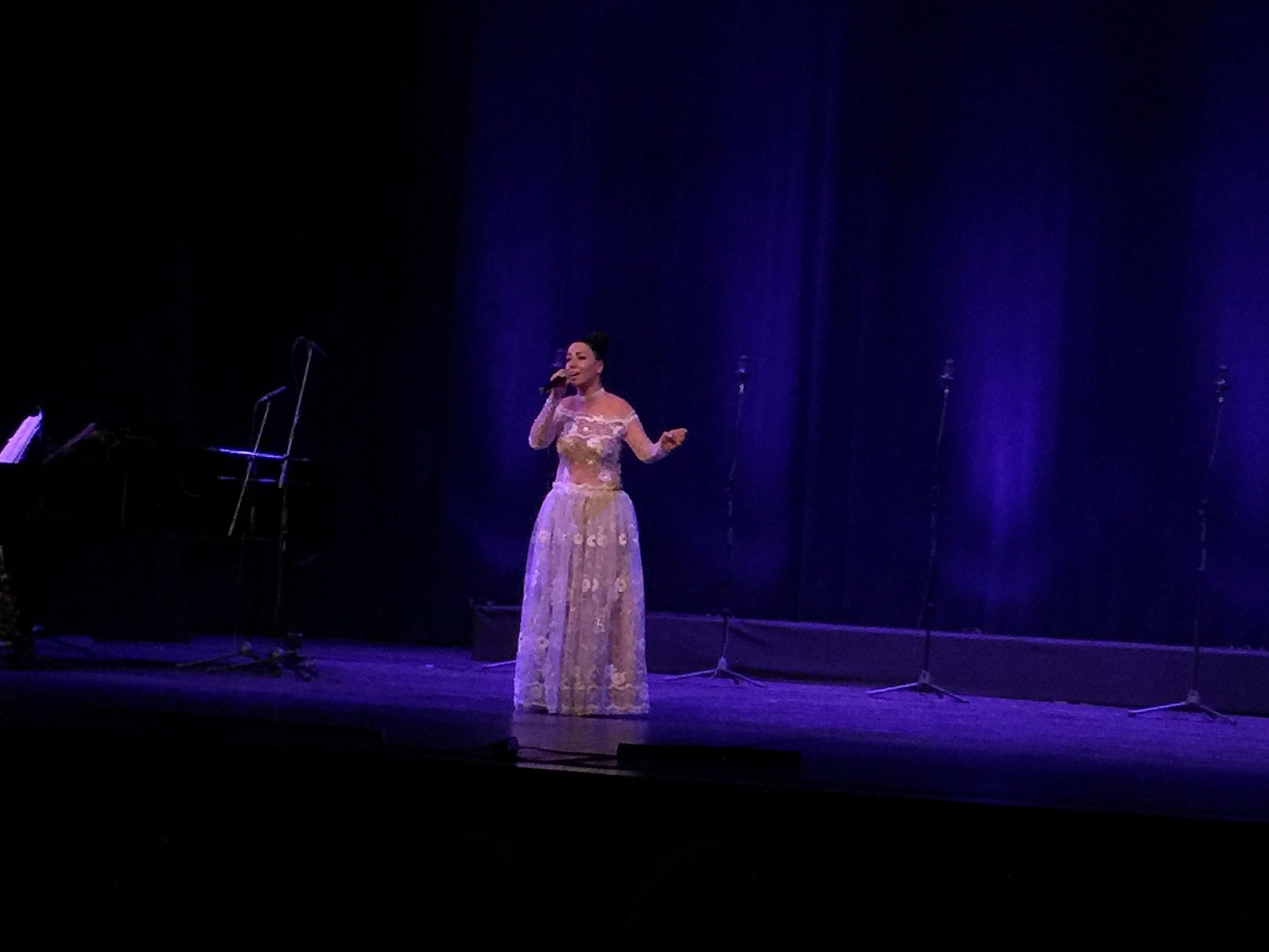 Chanteuse en récital devant un pupitre, partition ouverte et main posée sur le bord du piano