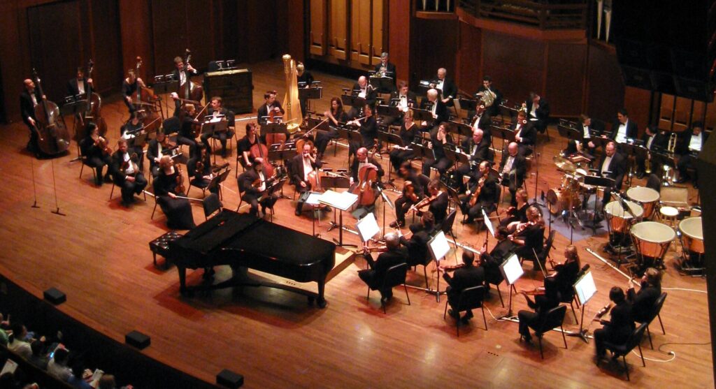 Orchestre symphonique installé sur scène, pupitres de cordes à gauche et cuivres au fond