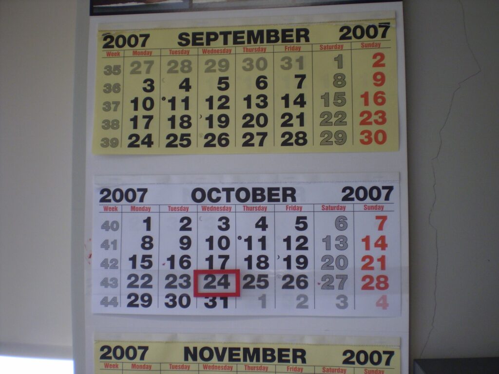Calendrier mural ouvert sur un mois entier, cases annot&eacute;es au stylo pr&egrave;s d'une fen&ecirc;tre