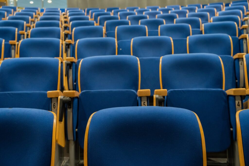 Rangées de fauteuils vides vues depuis le fond d'une salle, scène éclairée au loin
