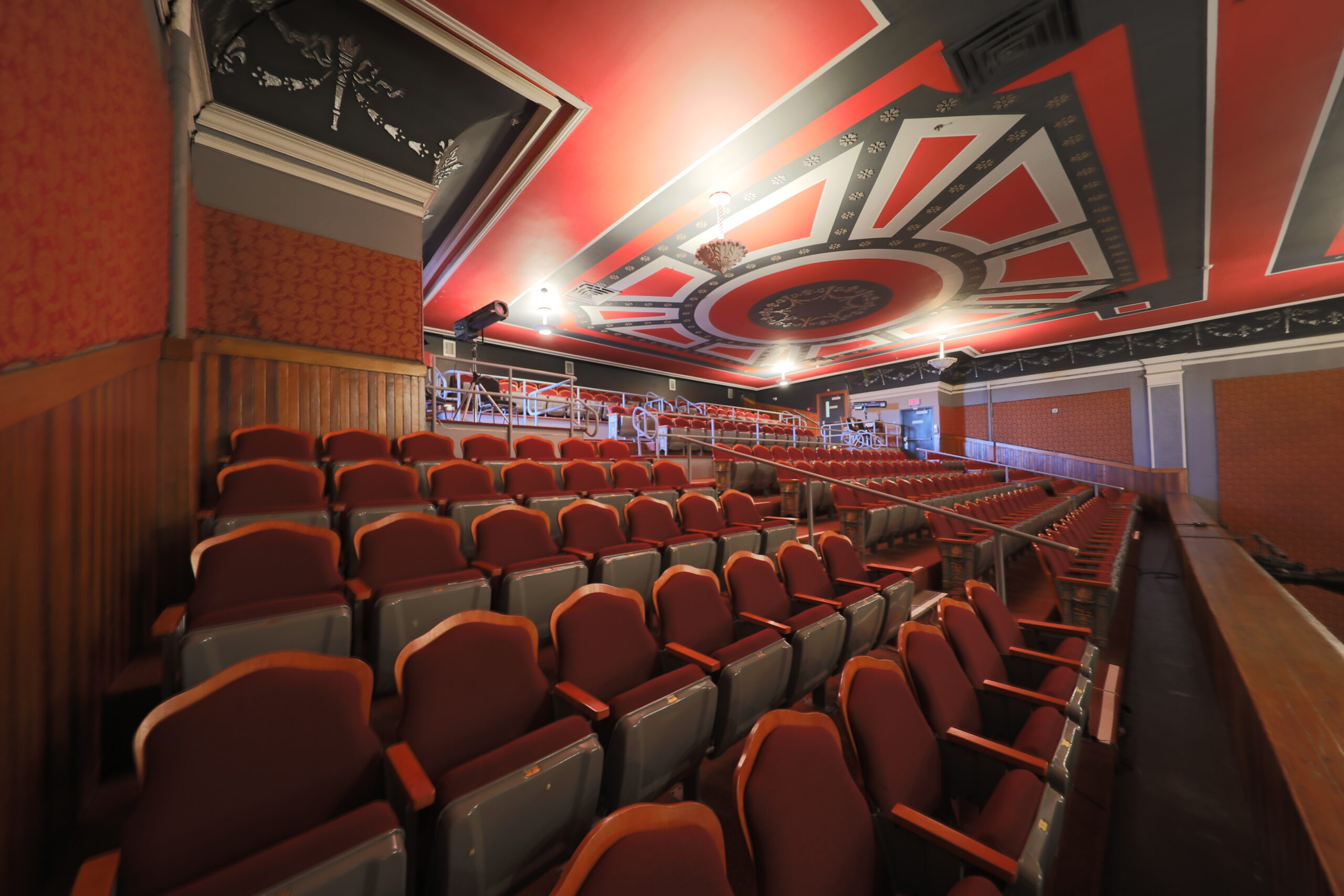 Balcon d'une salle de spectacle avec ses rangées de fauteuils et sa rambarde de bois sculpté