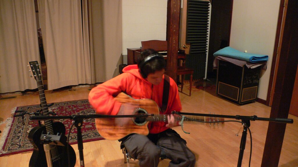 Micro sur pied dirigé vers le manche d'une guitare tenue par un musicien assis