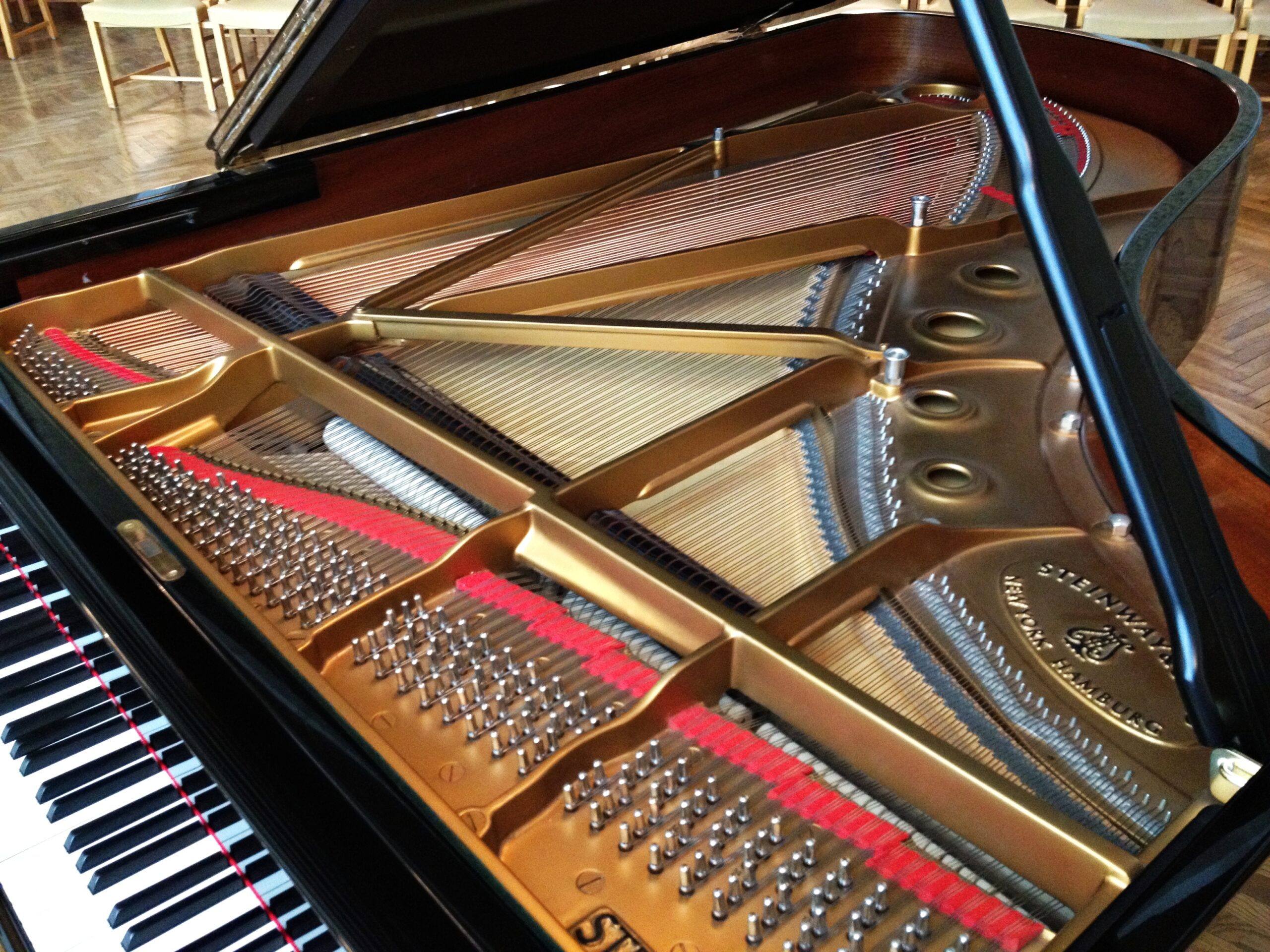 Piano à queue seul sur une estrade vide, couvercle levé, dans une salle faiblement éclairée