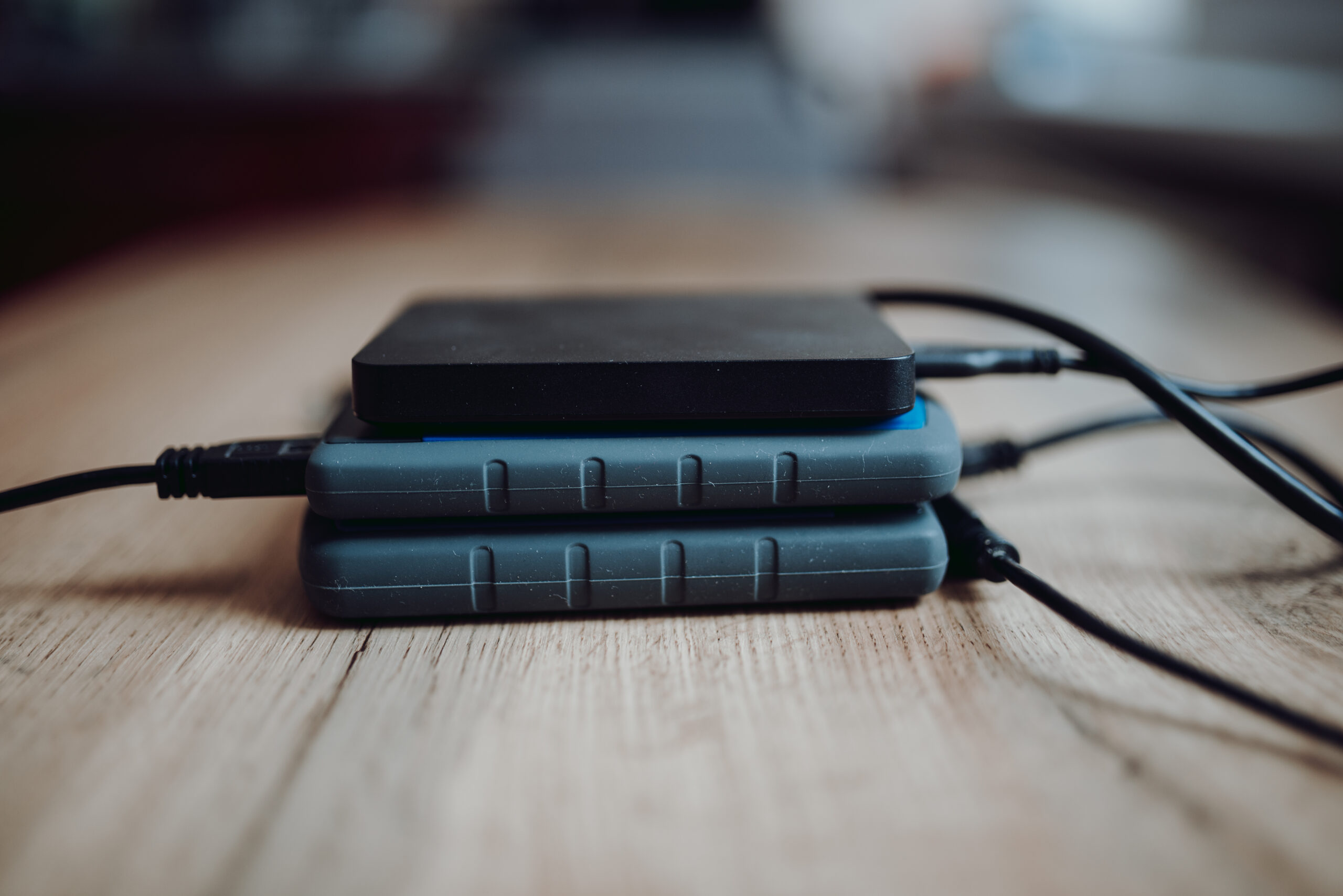 Plusieurs disques durs externes empilés sur un bureau, câbles USB visibles
