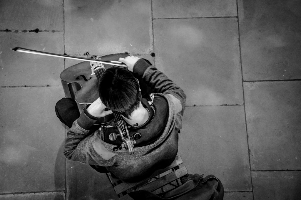 Violoncelliste assis dans une pi&egrave;ce d'habitation, archet pos&eacute; sur la corde grave